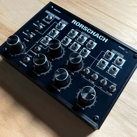 Rorschach video synthesizer on a wooden table, showing its knobs, switches and patch jacks